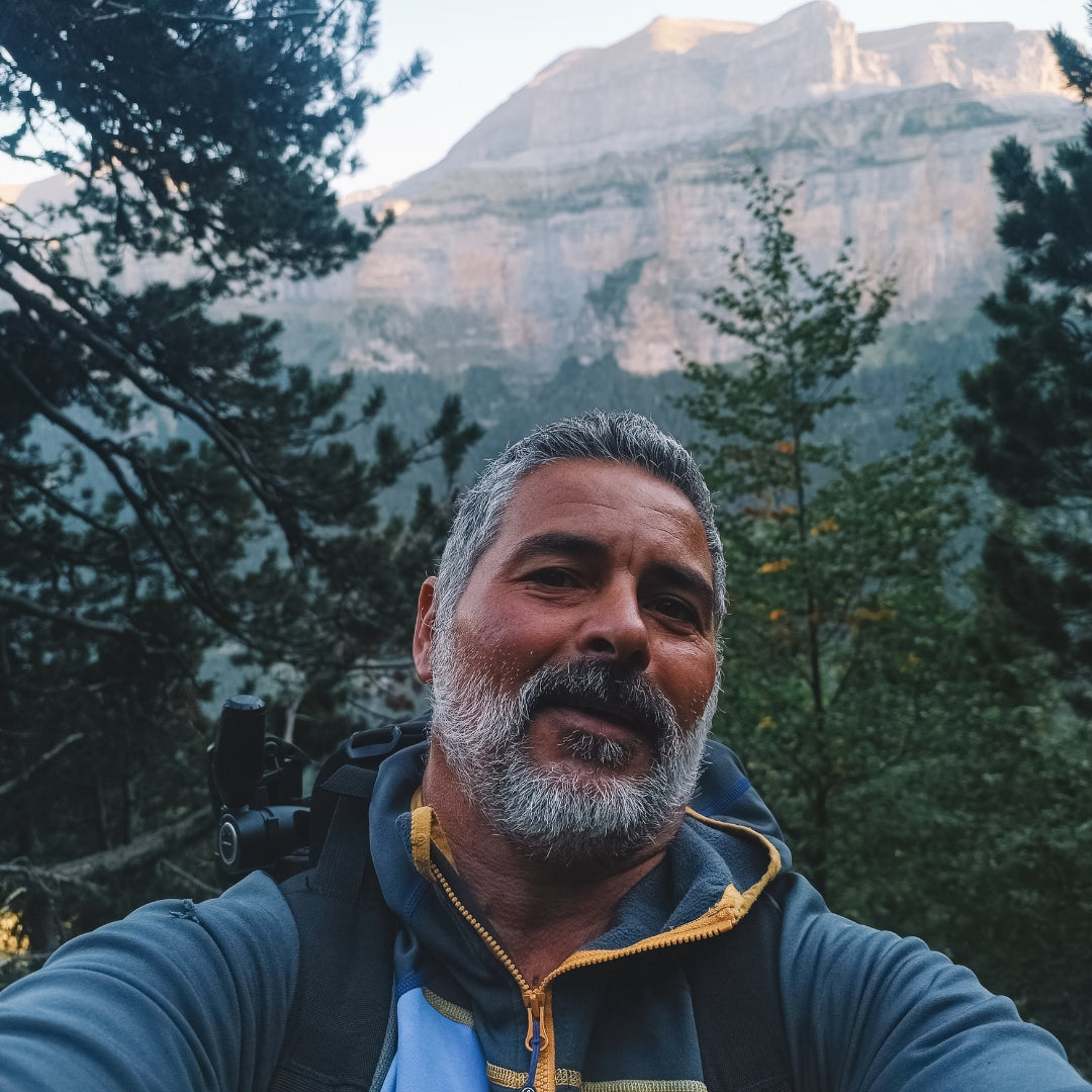 Man with a beard and mustache standing in front of a mountainous landscape