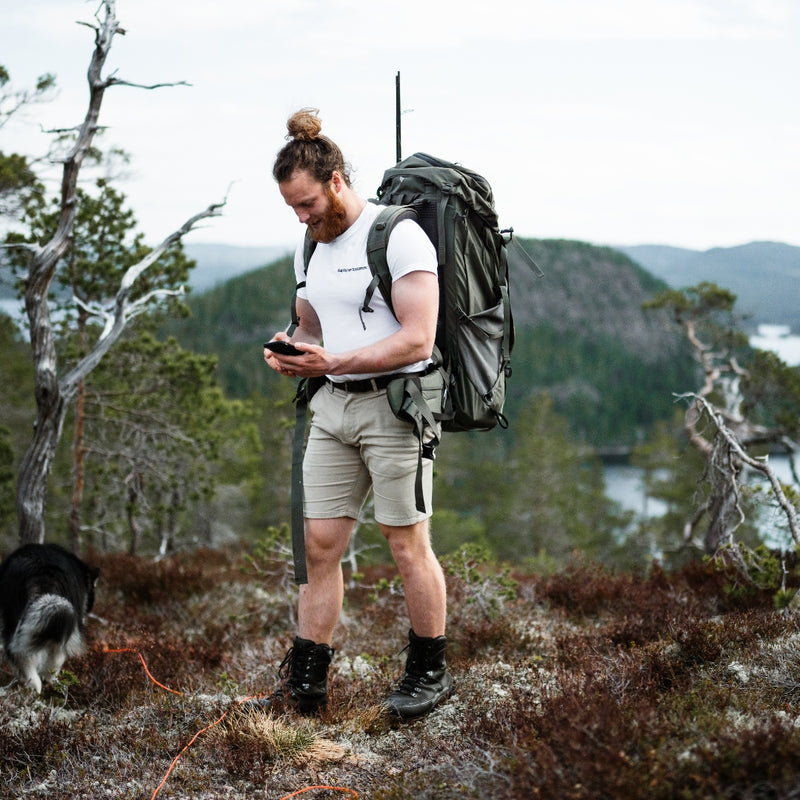 Male hiker with large backpack checking phone beside a small dog.