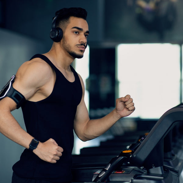 Man with headphones and fitness tracker running on a gym treadmill.