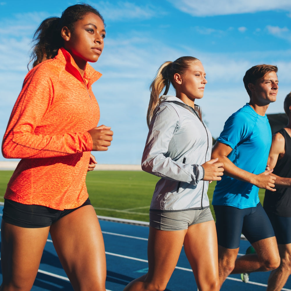 Three athletes in performance activewear running on a blue outdoor track.