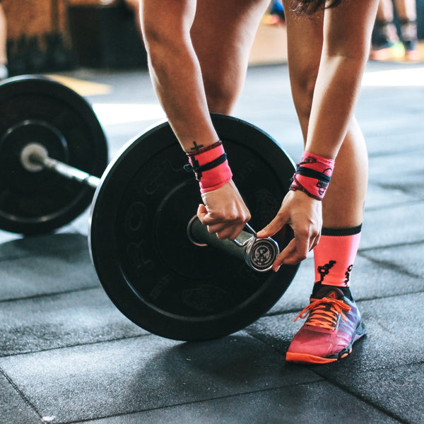 Female athlete with pink wrist wraps adjusting weights on a barbell.